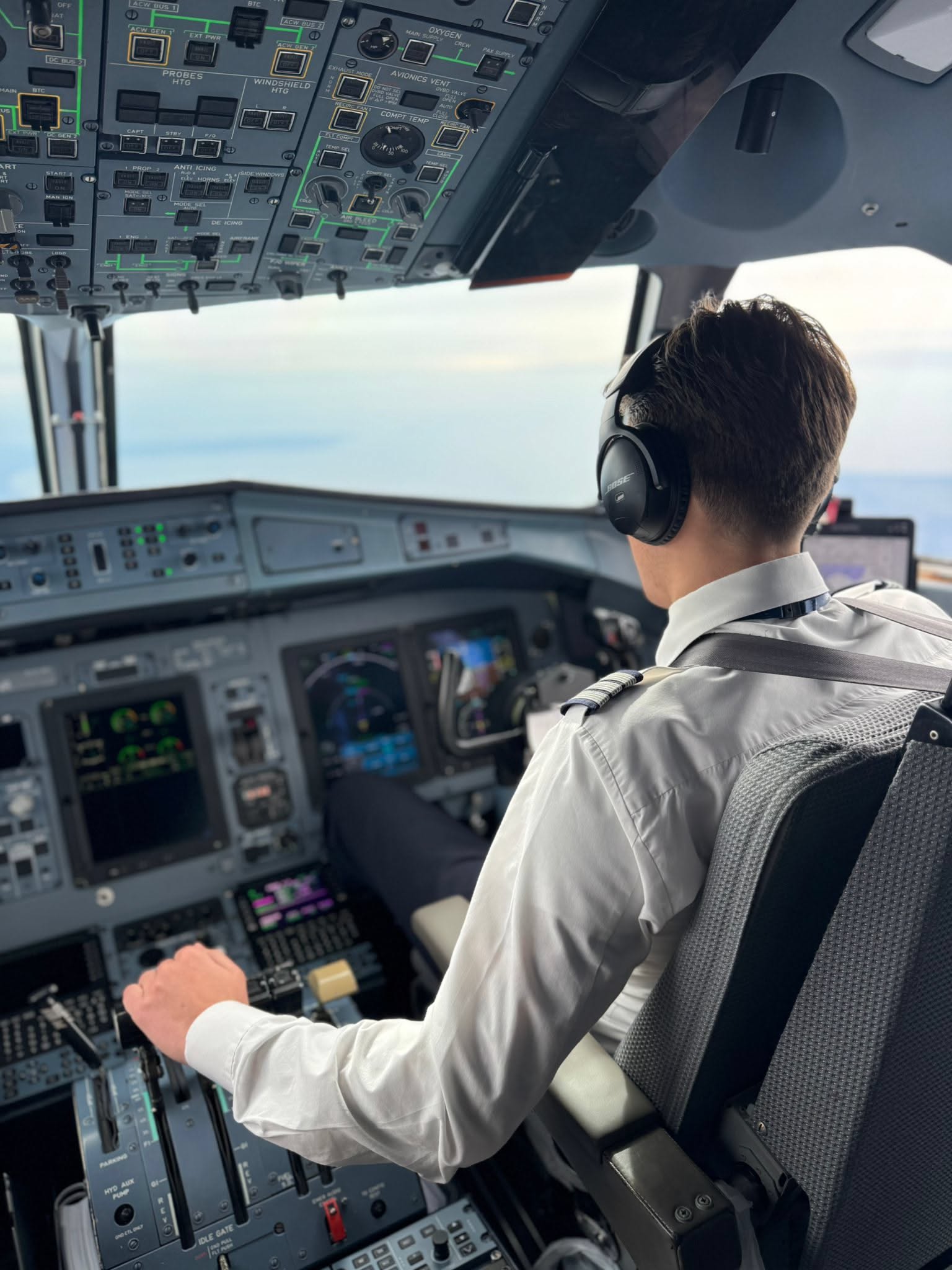 A first officer in the right seat of a regional airliner flight deck, hand on the thrust levers